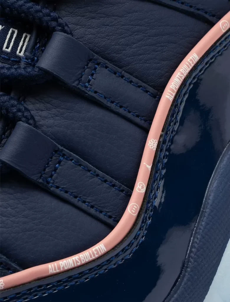 Close-up of navy leather ballet flats with braided trim and pink edging printed “ALL POINTS BULLETIN”