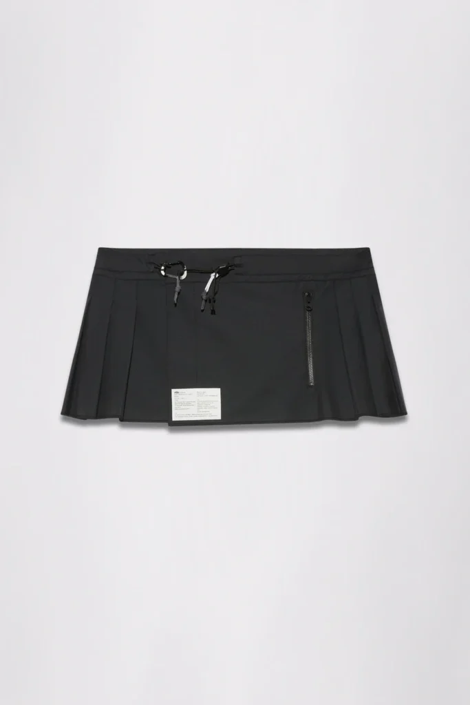 Black pleated mini skirt with drawstring waist, zippers, and a white rectangular label on a light background