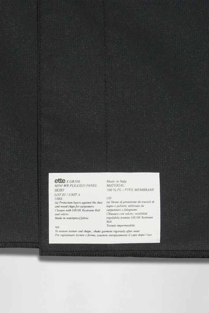 Black pleated fabric with a sewn-in white care label displaying small text