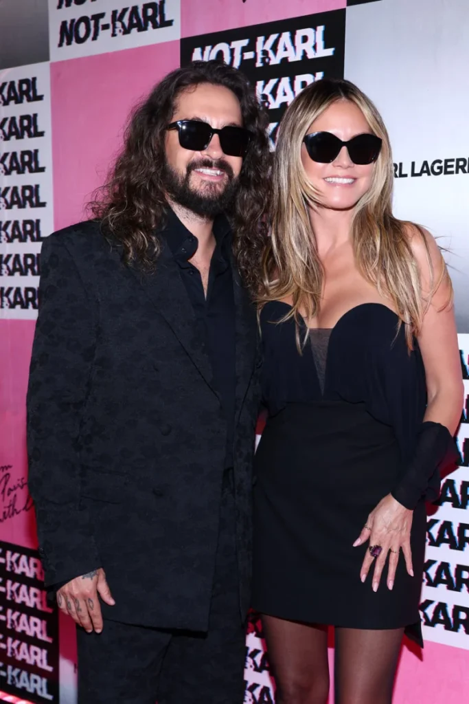 Heidi Klum and Tom Kaulitz pose in black outfits and sunglasses before a pink-and-black NOT-KARL backdrop