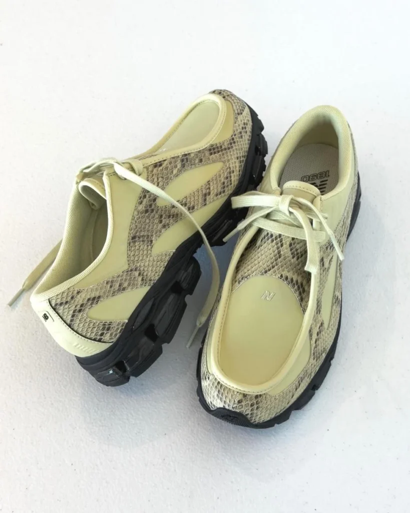 Pair of pale yellow New Balance shoe with snakeskin-patterned panels, laces, and black rugged soles on white background