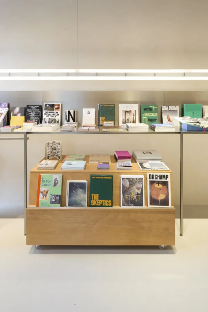 Display table of art books and magazines in a minimalist shop, with shelves of publications behind it