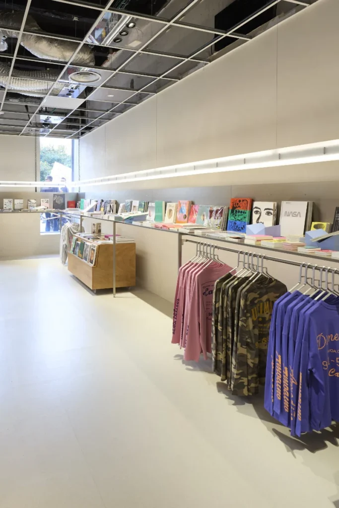 Bright minimalist shop interior with colorful magazines and clothing racks displaying pink, patterned, and purple shirts