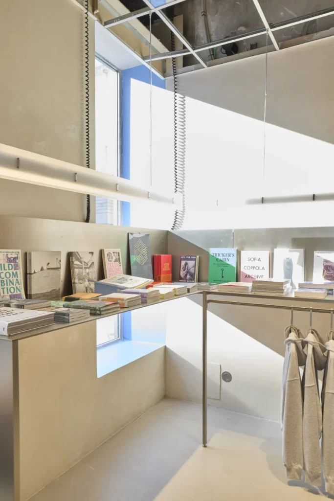 Bright minimalist shop interior with books and magazines on shelves, clothing on a rack, and large windows