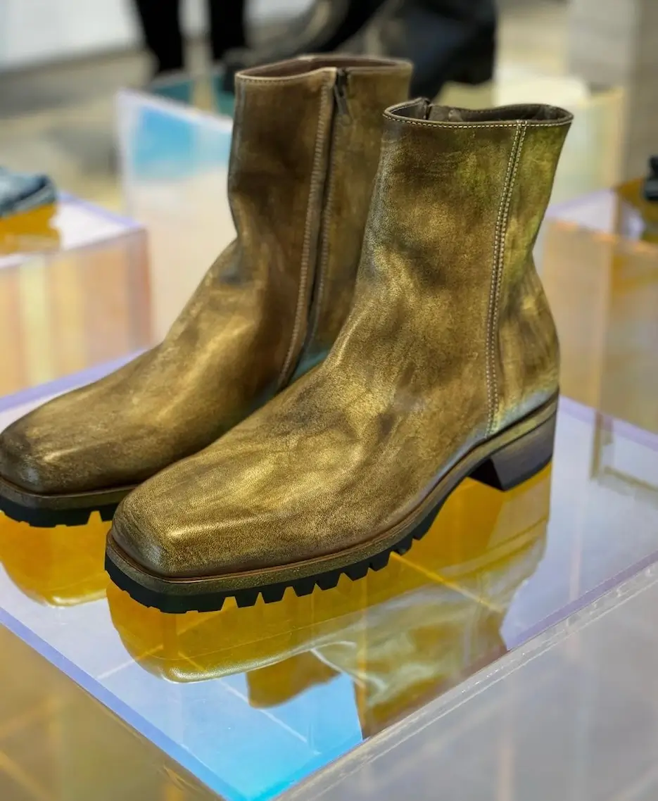 Pair of metallic gold ankle boots with square toes and thick black lug soles displayed on a mirrored platform