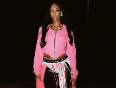 A'ja Wilson poses in a pink cropped zip jacket and black-and-white pants against a dark background