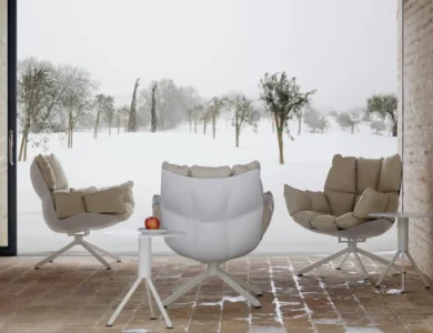 Three cushioned swivel lounge chairs frame a small white table with an apple, overlooking a snow-covered orchard through