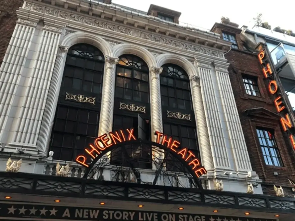 Ornate Phoenix Theatre facade with arched windows, sculpted columns, orange neon signage and a marquee reading “A New Story