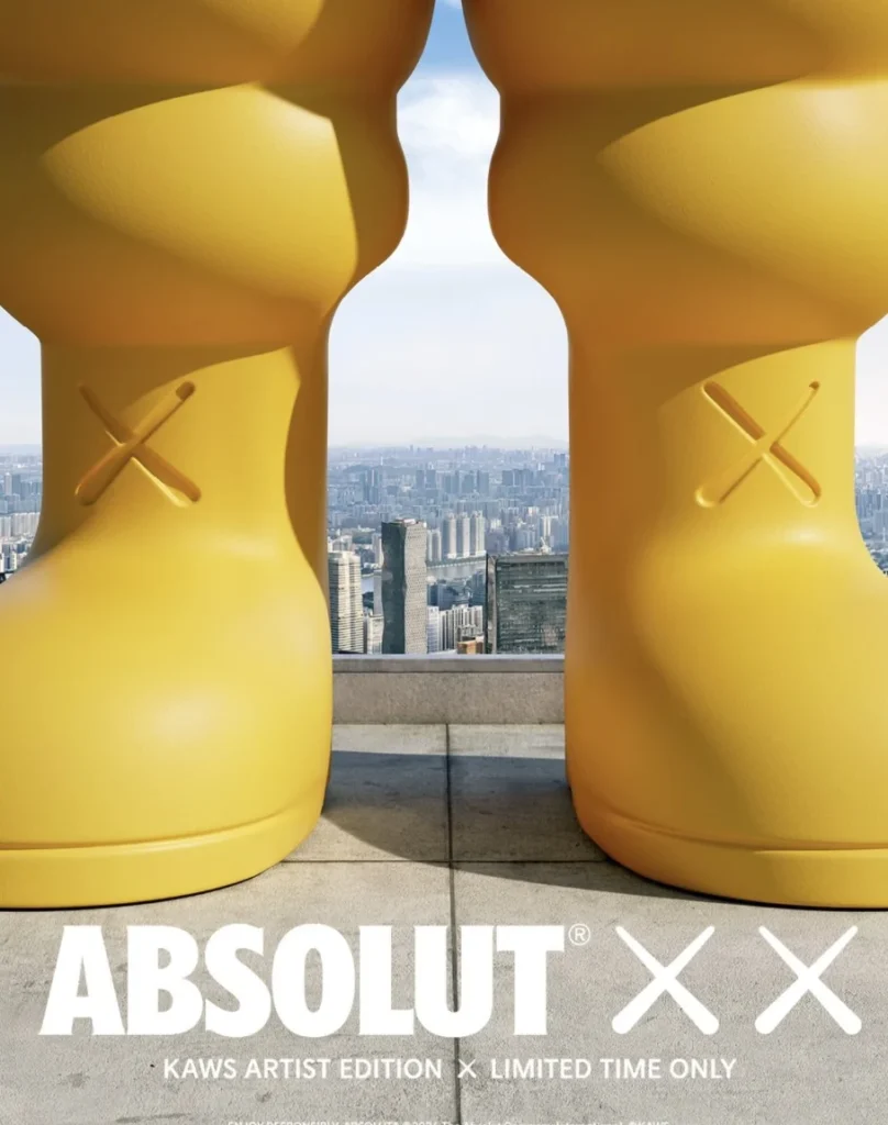 Two large yellow boot-shaped sculptures with crossed details overlook a dense city skyline from a rooftop terrace