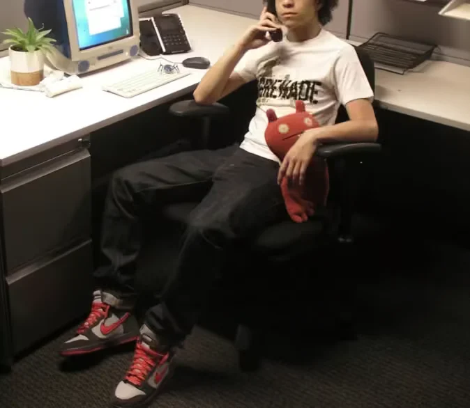 xaviersobased seated in an office chair, holding a red plush toy and a phone, wearing a white graphic T-shirt and red sneakers