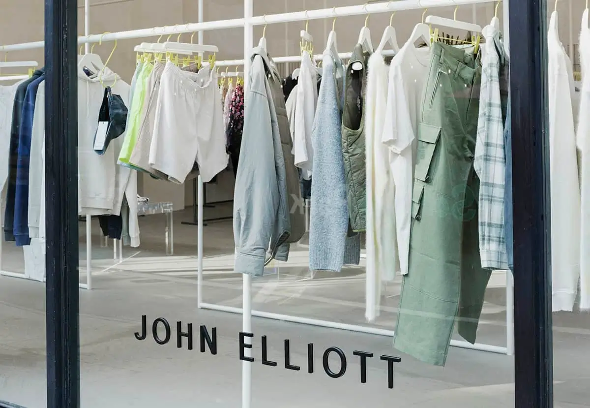 John Elliott clothing displayed on racks behind a storefront window