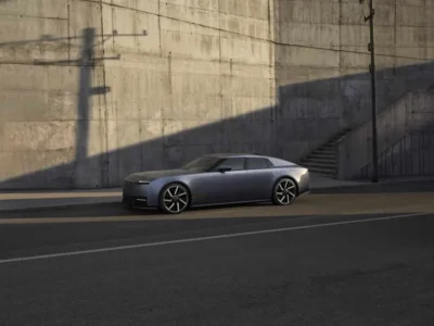 Silver-gray electric sedan parked beside a concrete wall and stairway, with large alloy wheels and sharp, angular styling