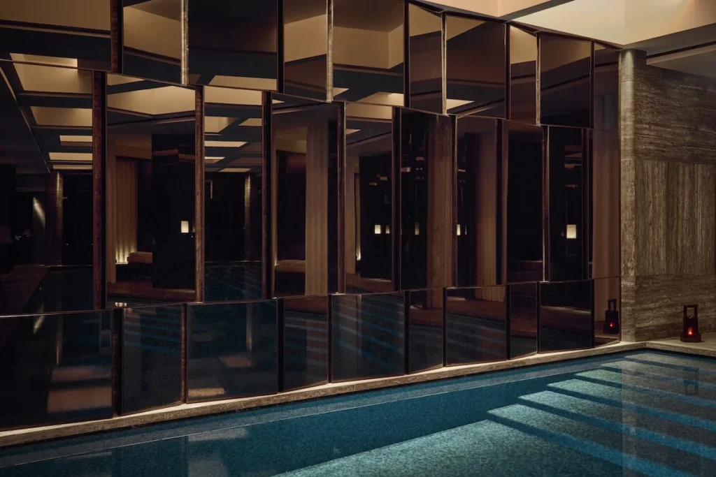 Dark, reflective spa interior with mirrored partitions and a blue-tiled pool edged by stone flooring