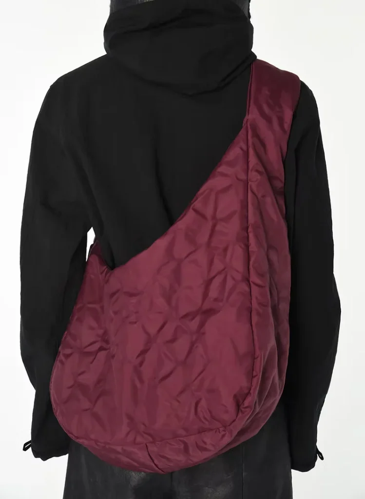 Person seen from behind wearing a black hooded jacket and carrying a large burgundy quilted shoulder bag