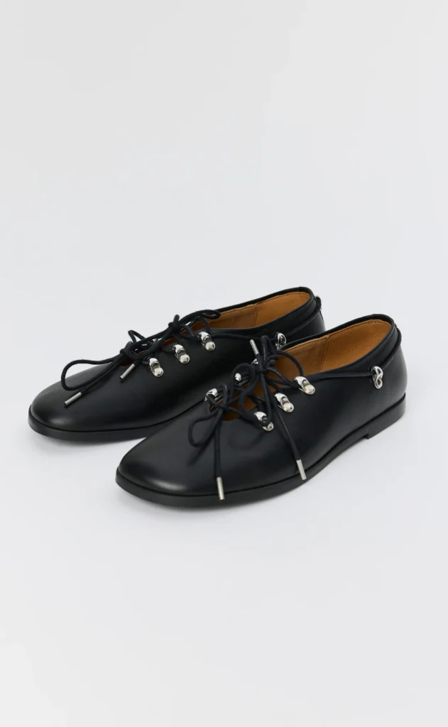 Pair of black leather lace-up shoes with silver eyelets and tan lining on a white background