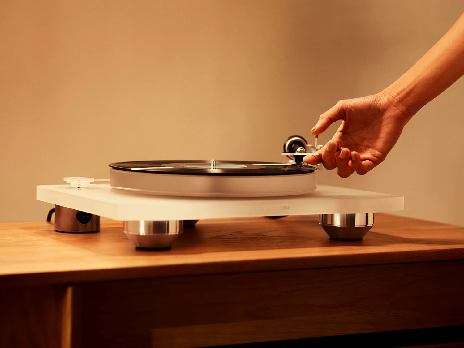 Hand adjusting the tonearm of a white turntable on a wooden table