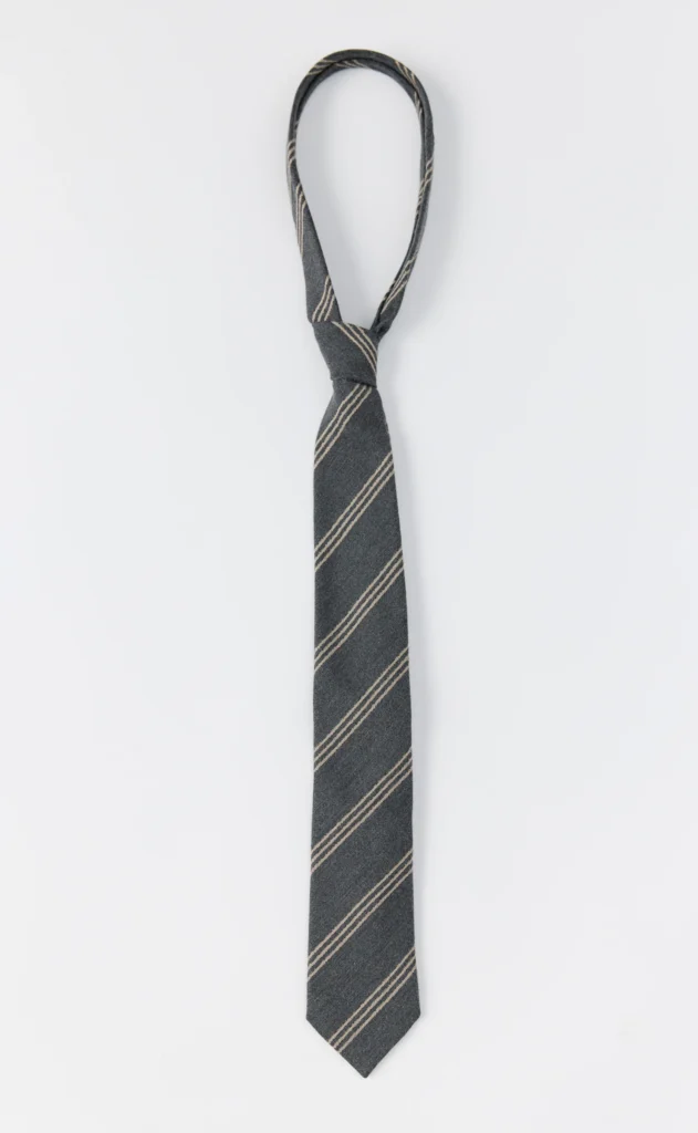 Dark gray necktie with thin beige diagonal stripes, knotted and laid vertically on a white background