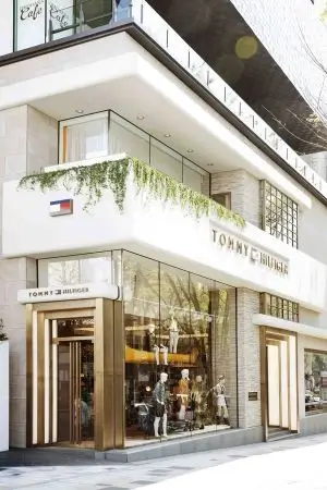 Tommy Hilfiger storefront with white facade, hanging greenery, glass entrance, mannequins, and sidewalk in Tokyo