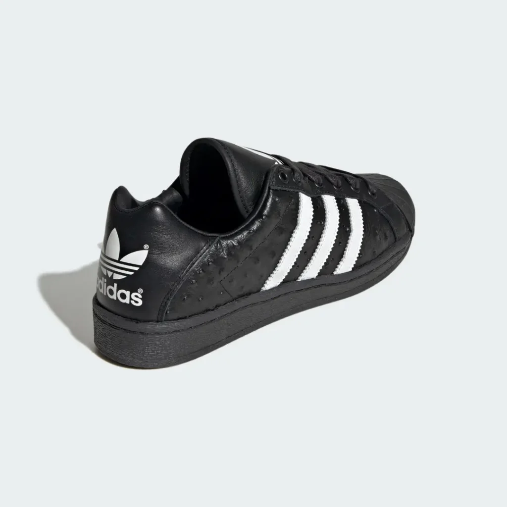 Black Adidas sneaker with white three stripes and trefoil logo, shown at an angle against a pale background