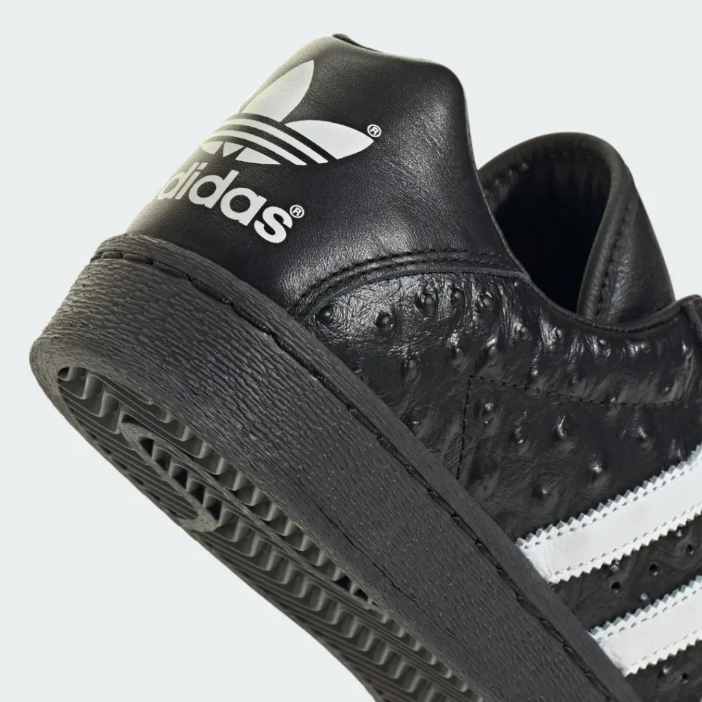 Close-up of a black adidas sneaker with white branding and stripes, textured rubber sole, and pebbled leather upper on a