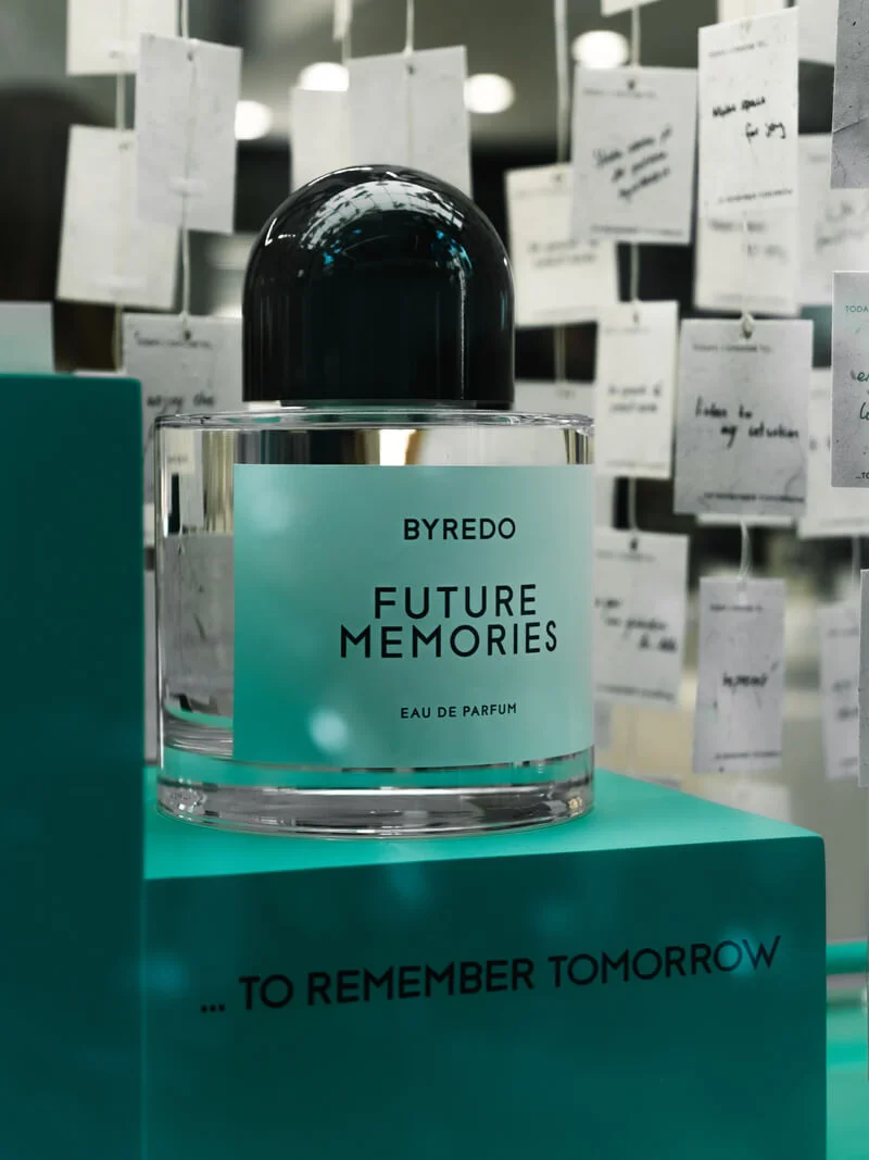 Byredo Future Memories perfume bottle on a teal pedestal, surrounded by hanging handwritten notes