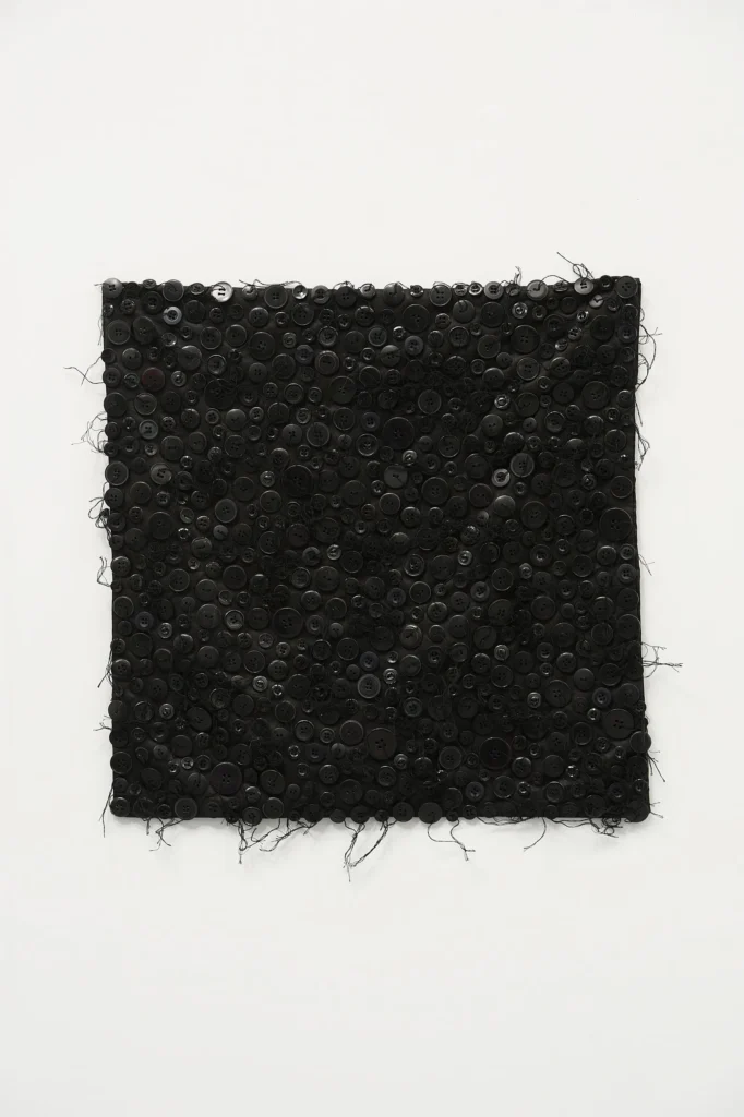 Rectangular black textile panel densely covered with buttons and loose threads, isolated against a white background