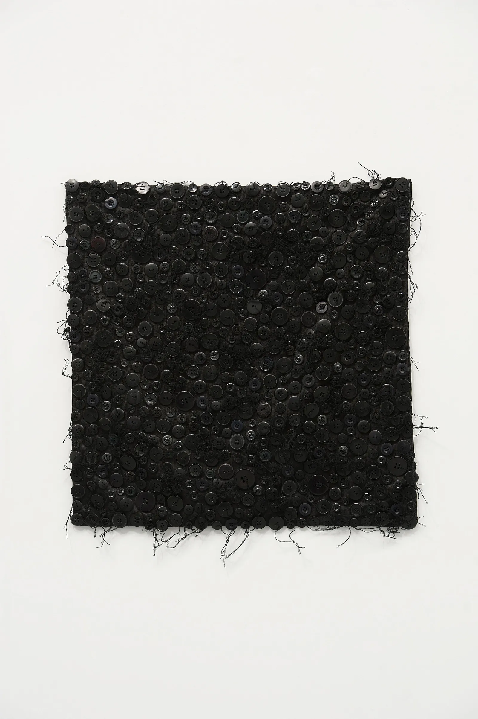 Rectangular black textile panel densely covered with buttons and loose threads, isolated against a white background
