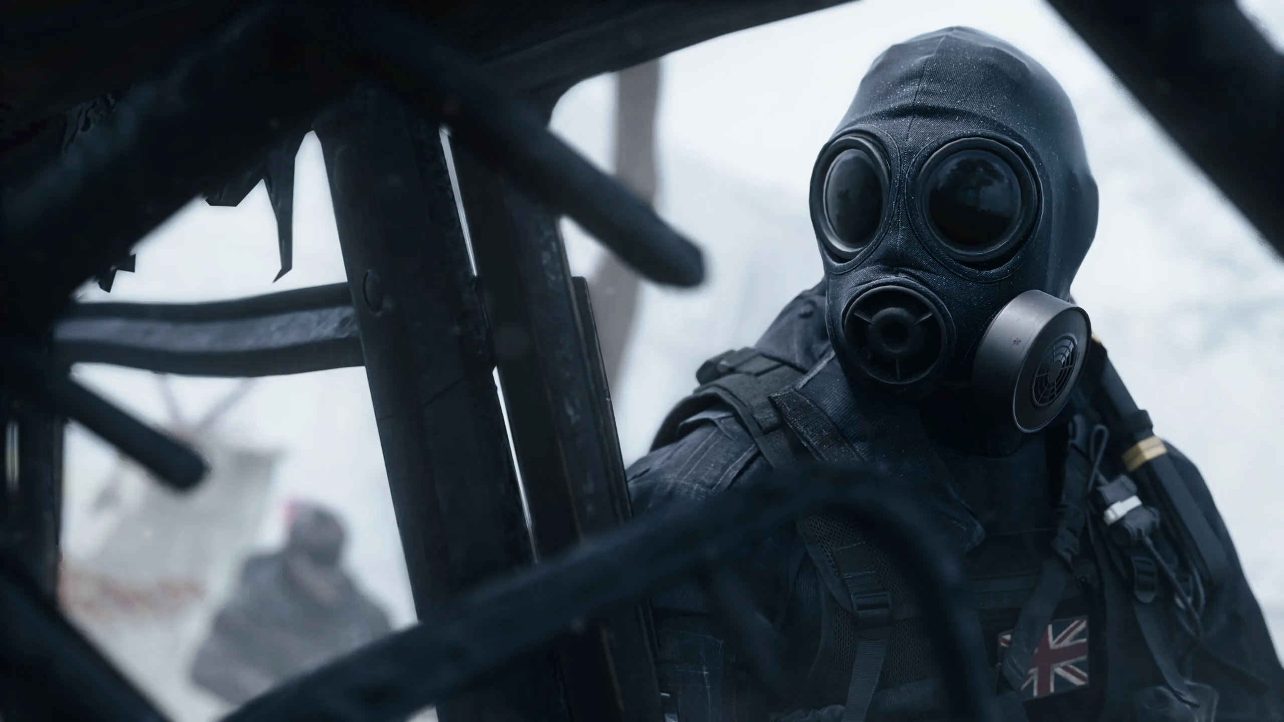 Masked soldier in black tactical gear and Union Jack patch, viewed through dark aircraft framework against a bright sky