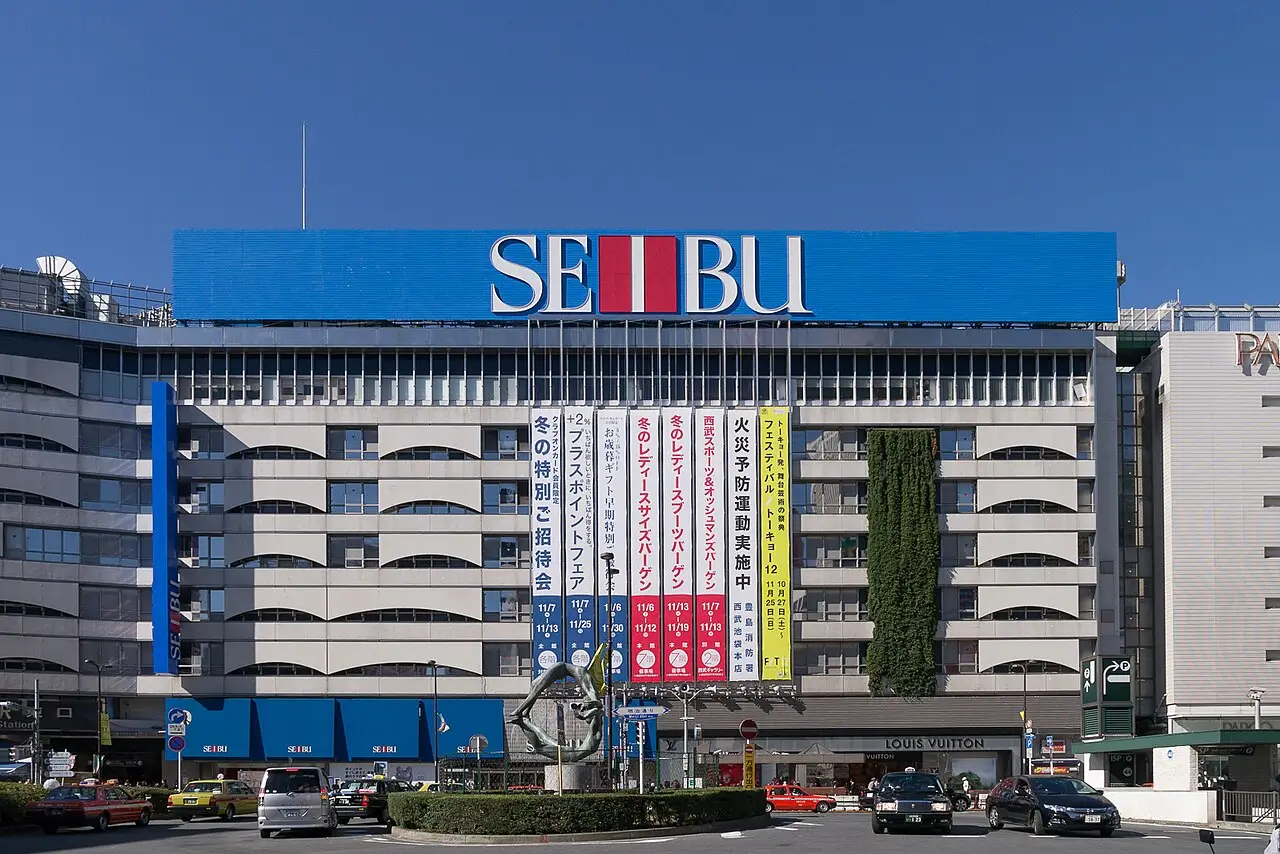 Seibu department store facade with large blue sign, Japanese banners, street traffic, and a sculpture in the foreground