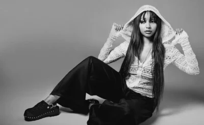 PinkPantheress sits on the floor in a lace hooded top, wide black pants and studded platform shoes