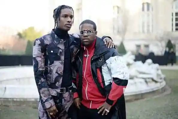 A$AP Rocky and Ferg pose together outdoors, wearing patterned and red-and-black jackets in front of a fountain