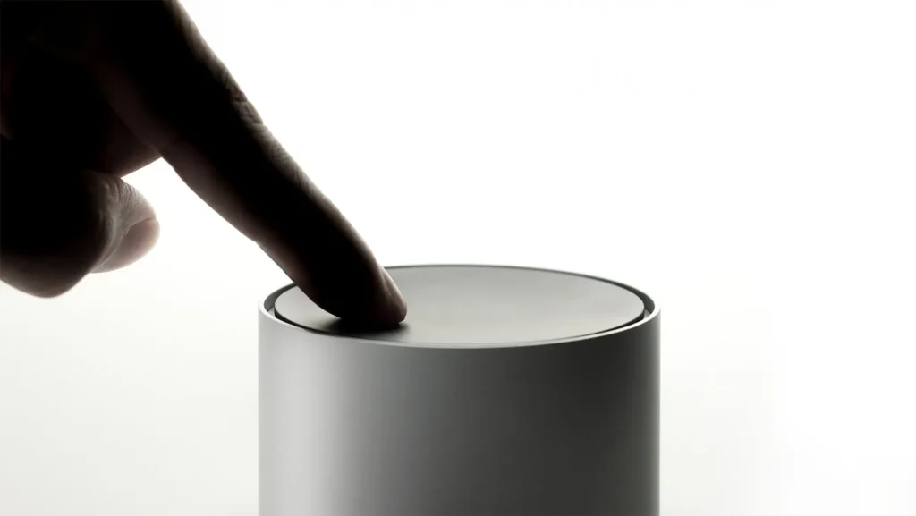 Finger pressing the top of a cylindrical gray diffuser against a white background