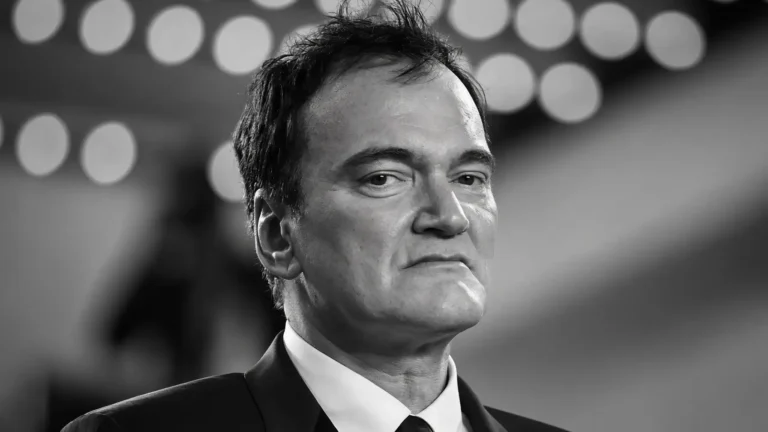 Close-up black-and-white portrait of Quentin Tarantino in a suit, with blurred circular theater lights behind him