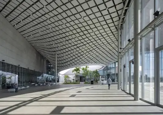 Spacious modern factory atrium with a gridded glass roof, glass walls, polished floor and a lone person walking through it