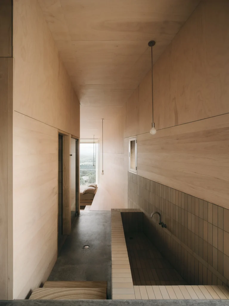 Wood-lined bathroom with a sunken tiled bathtub, pendant lights, concrete floor and mountain views through a window