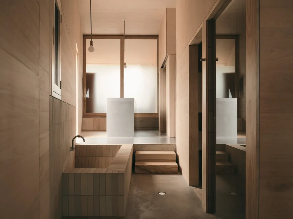 Warm-toned bathroom with a tiled sunken tub, freestanding white basin, wood walls, steps, pendant lights, and mirrored