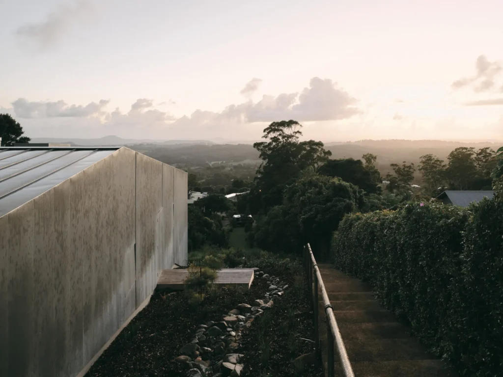 Zinc-clad pavilion beside a garden path overlooks a wooded valley and distant mountains at sunset