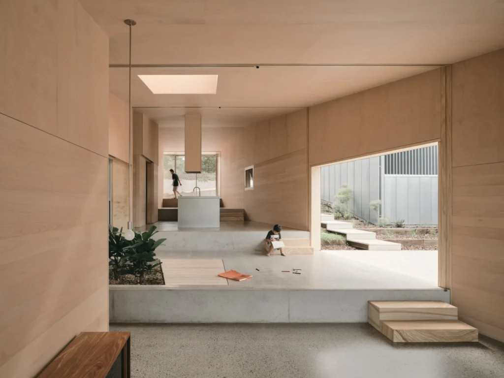 Minimalist wood-lined living space with concrete steps, skylight, plants, and a child near an open courtyard