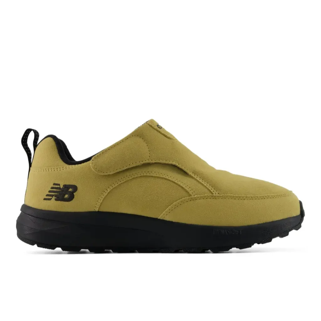 Mustard-yellow New Balance sneaker with black logo, thick black sole, and strap-like upper detail on white background