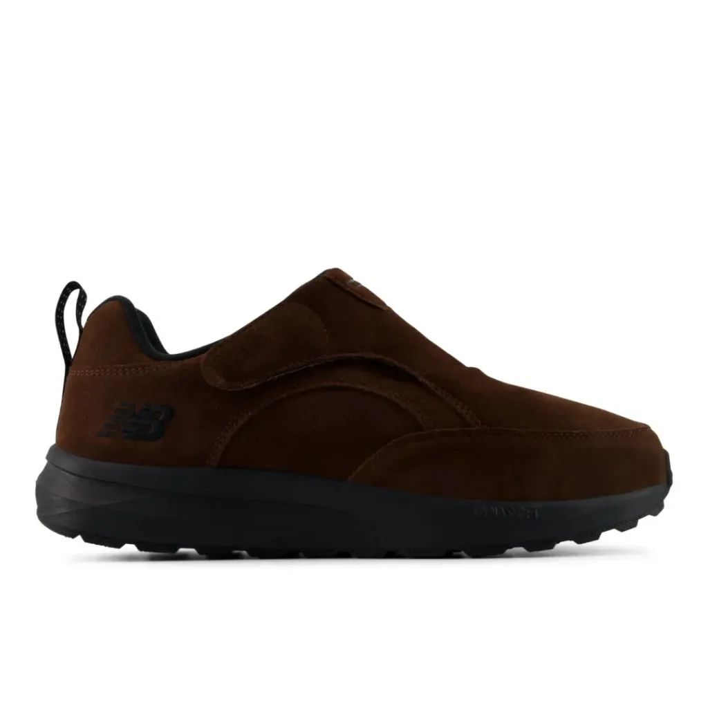 Brown New Balance slip-on sneaker with a strap, black sole, and heel pull tab against a white background