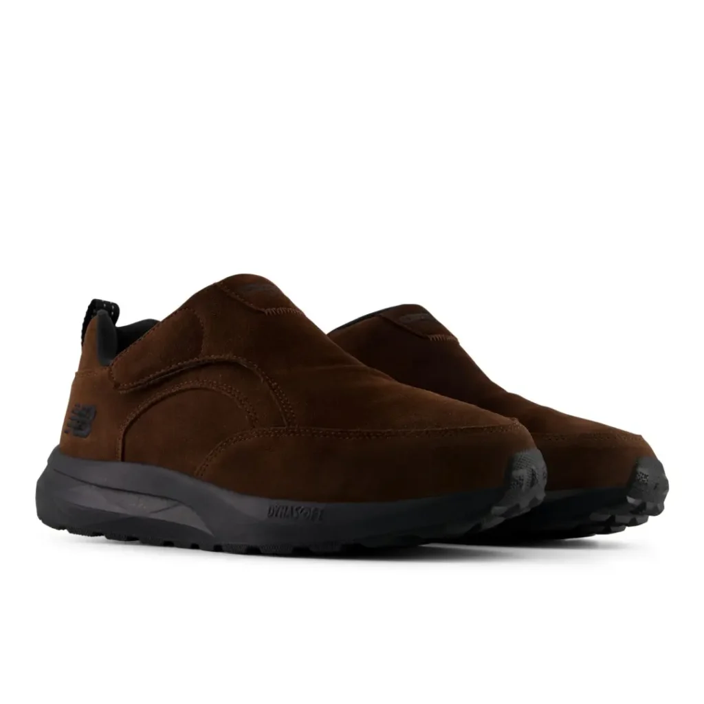 Pair of brown suede New Balance slip-on shoes with black midsoles and rugged soles on a white background