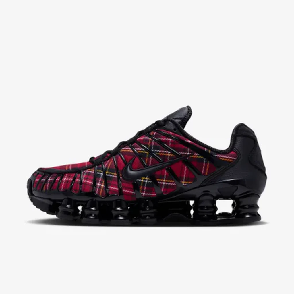Black Nike Shox sneaker with red plaid fabric panels, black overlays, and a segmented raised sole on a white background