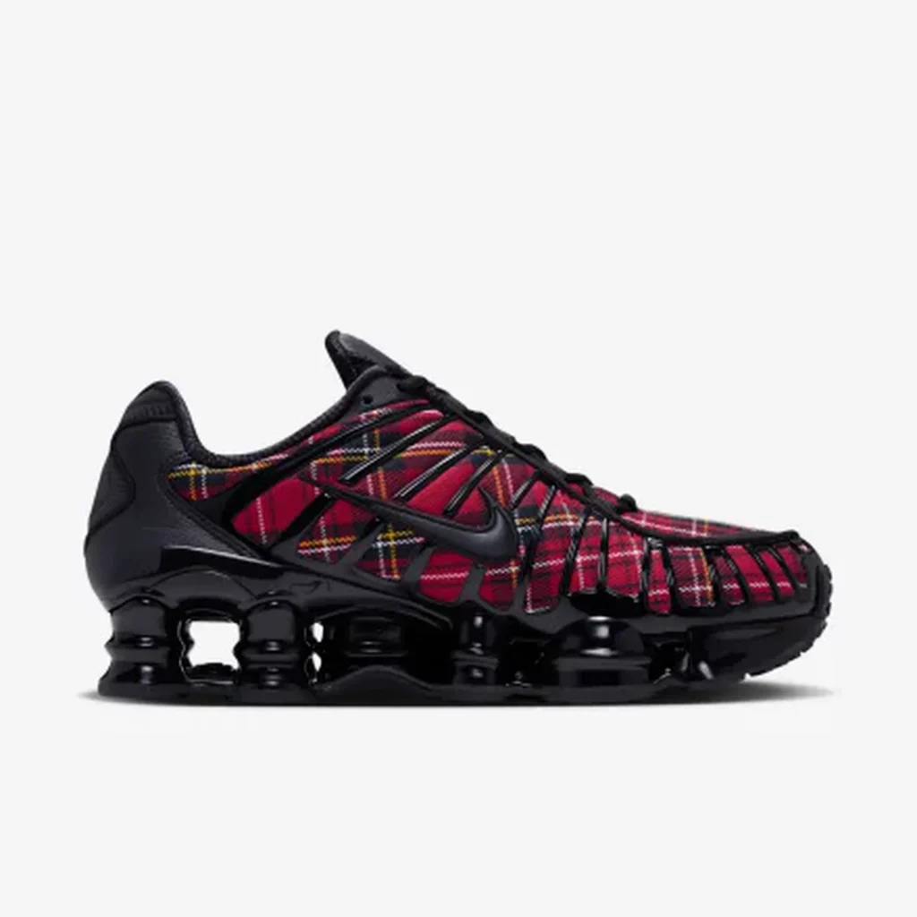 Black Nike Shox sneaker with red-and-yellow plaid panels, black cage overlays, and segmented sole on a white background