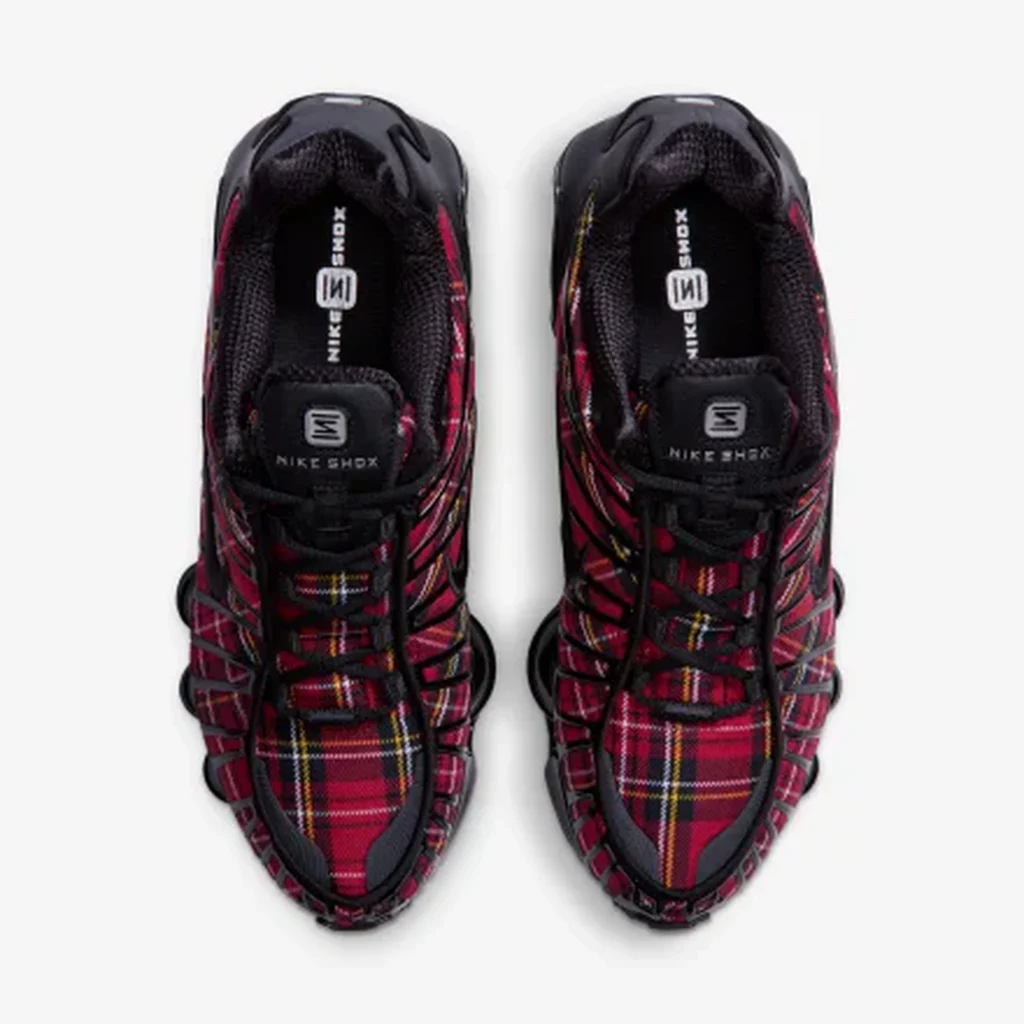 Top-down view of black sneakers with red tartan plaid panels, multicolor stripes, and visible Nike Shox branding on a white