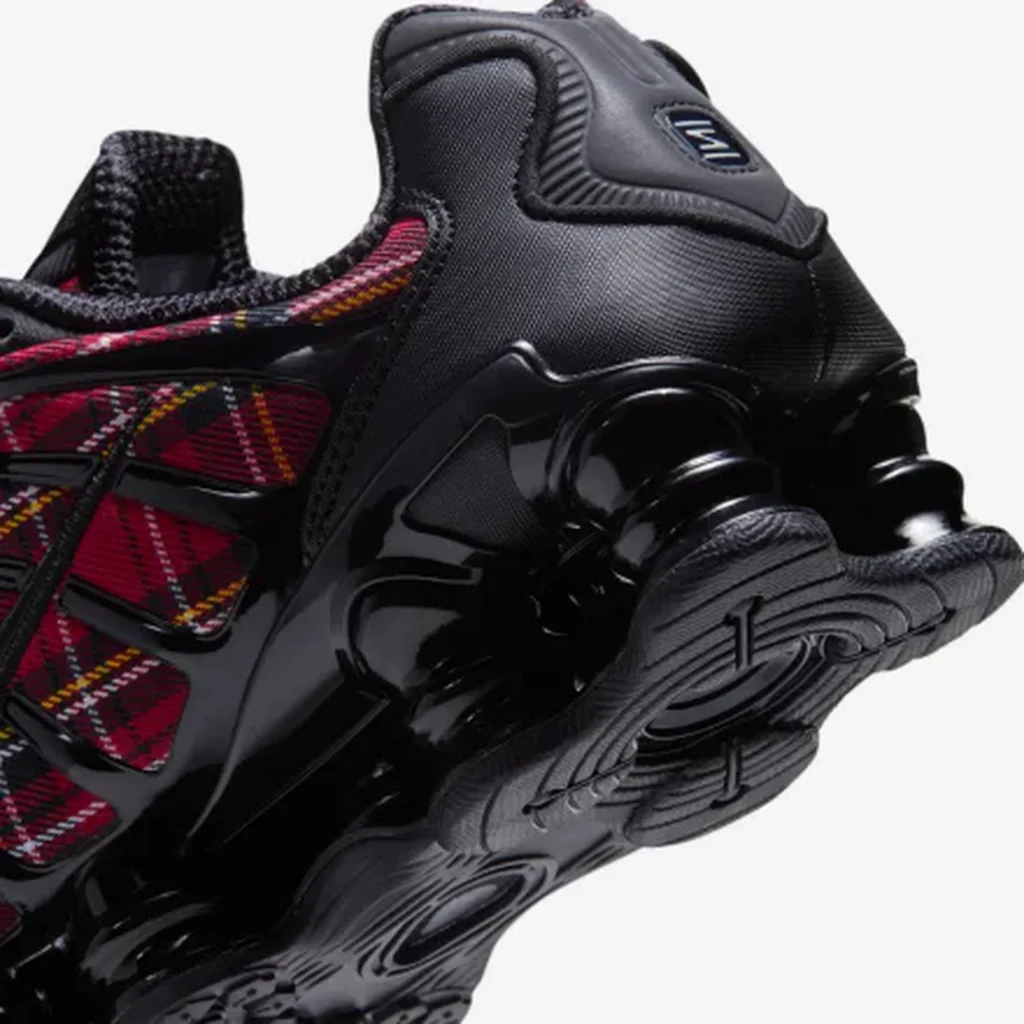 Close-up of black Nike Shox sneakers with red, yellow and white plaid panels, glossy black supports, and sculpted soles on