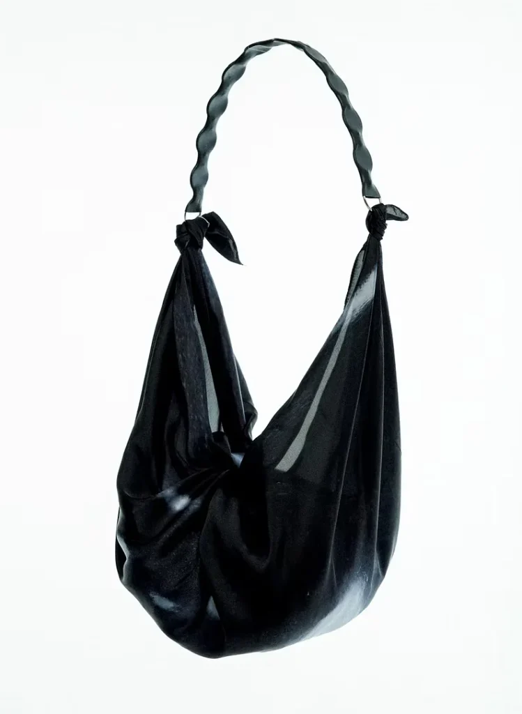 Black glossy leather shoulder bag with a twisted handle and knotted sides, isolated against a white background