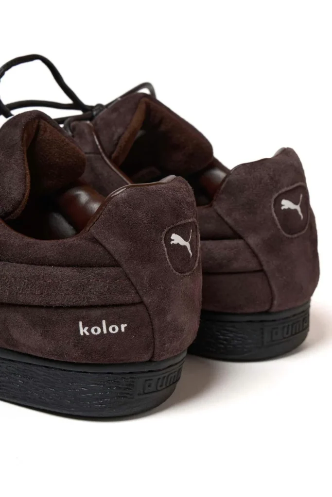 Pair of dark brown suede Puma shoe viewed from the rear, with black soles and white logos on a white background