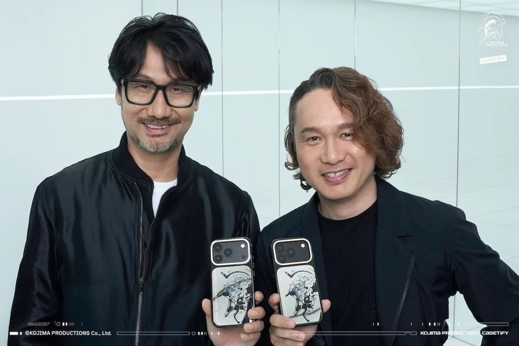 Two men hold matching phone cases with silver camera surrounds and black-and-white illustrated designs in a bright interior